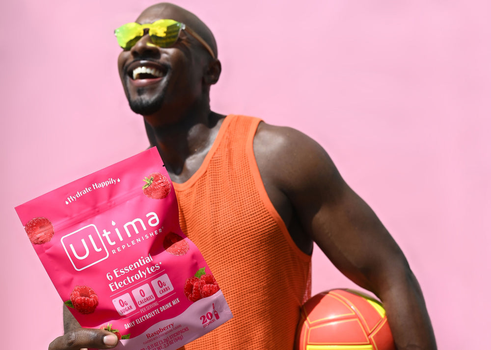 Man outside with ball holding up Ultima Replenisher Raspberry Electrolyte Powder Stickpacks