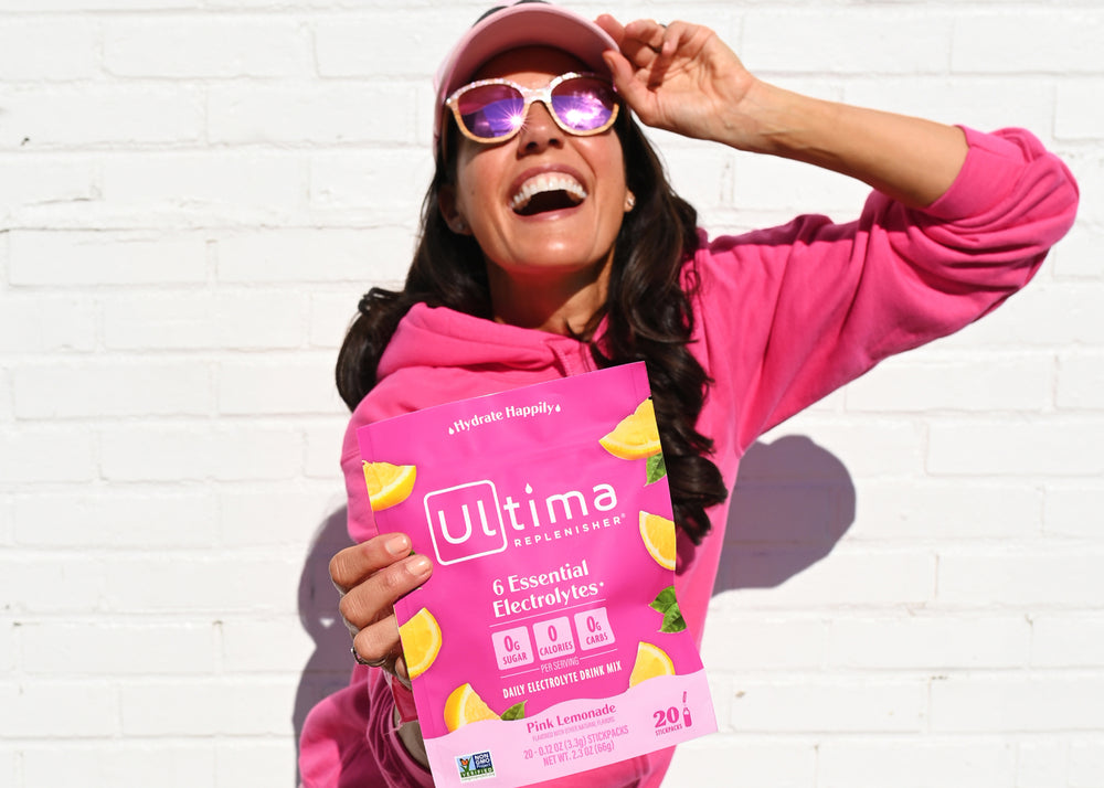 Woman in pink holding Ultima Replenisher Pink Lemonade Stickpacks Electrolyte Powder